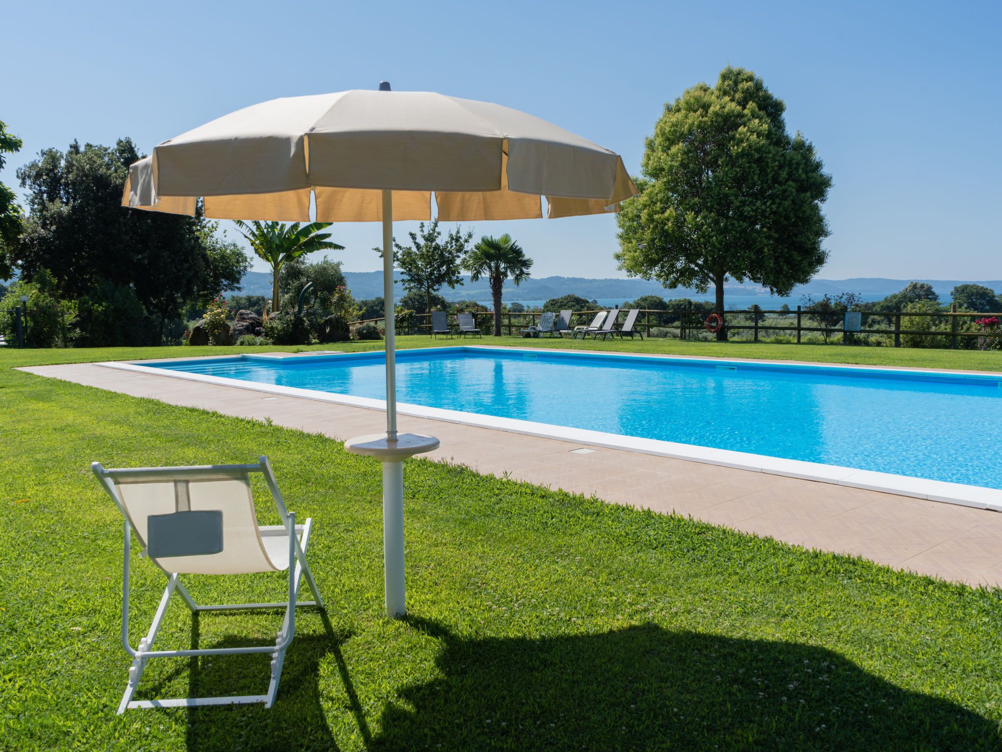 Une piscine avec un transat et un parasol, entourée d’arbres et offrant une vue sur le paysage.