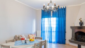 A dining area with a table set for four, a chandelier, a fireplace, and a blue curtain.