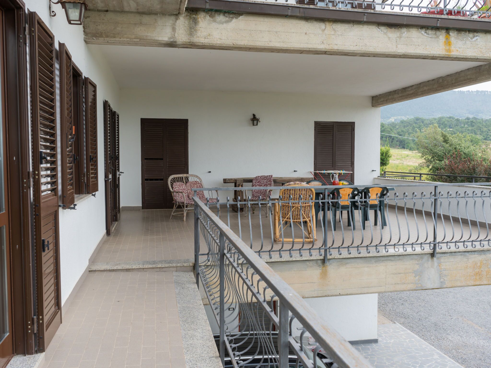 Un balcon avec une table et des chaises, une vue sur la campagne et un bâtiment doté de volets en bois.