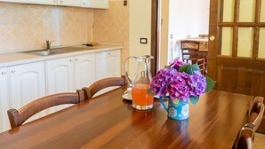 A kitchen with white cabinets, a sink, and a wooden table with chairs. There is a pitcher and a vase with flowers on the table. - Rosa Tea by Interhome (Lago di Bolsena)