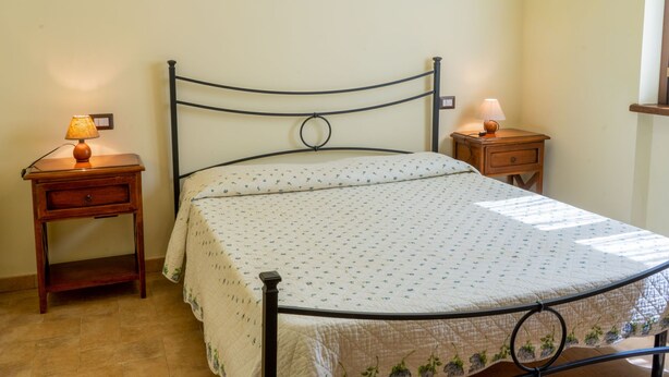 Une chambre à coucher avec un lit, une table de chevet avec une lampe, une autre table de chevet avec une lampe, et un tableau encadré accroché au mur.