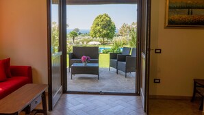 An open sliding glass door leading to an outdoor patio with wicker furniture, a red sofa, and a small table with flowers. - Rosa Tea by Interhome (Lago di Bolsena)