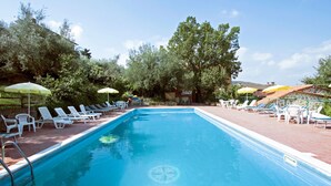 A swimming pool with lounge chairs and umbrellas, surrounded by trees and a stone building. - Vacanza L'Olivo by Interhome (Lago Trasimeno)