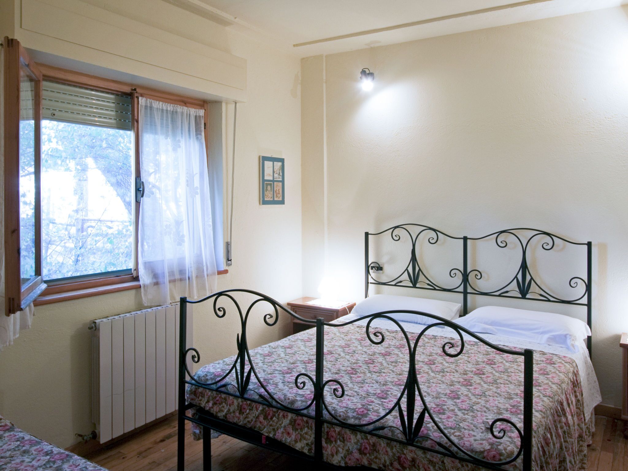 Um quarto com cama, janela com cortinas, radiador e luminária fixada na parede.
