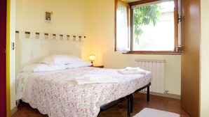 A bedroom with a bed, a nightstand with a lamp, a window with a view of greenery, and a radiator. - Vacanza L'Olivo by Interhome (Lago Trasimeno)