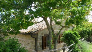 Un bâtiment en pierre, avec un toit recouvert de tuiles, entouré de verdure et d’une clôture en bois.