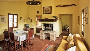 Un coin repas avec une table dressée pour quatre personnes, une cheminée et un canapé dans une pièce chaleureuse aux murs jaunes, baignée d’une lumière douce.