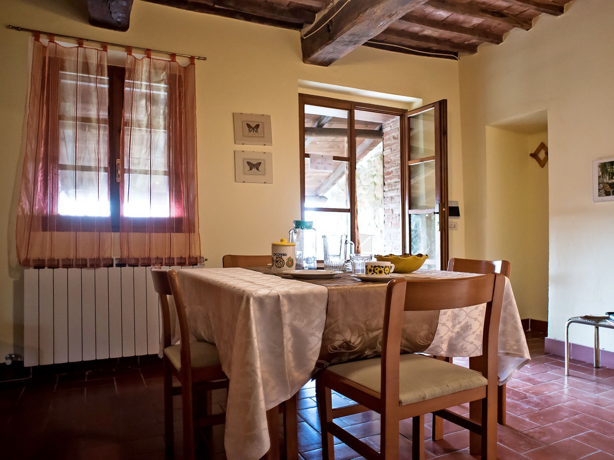 A dining area with a table set for two, wooden chairs, a radiator, and a window with curtains.
