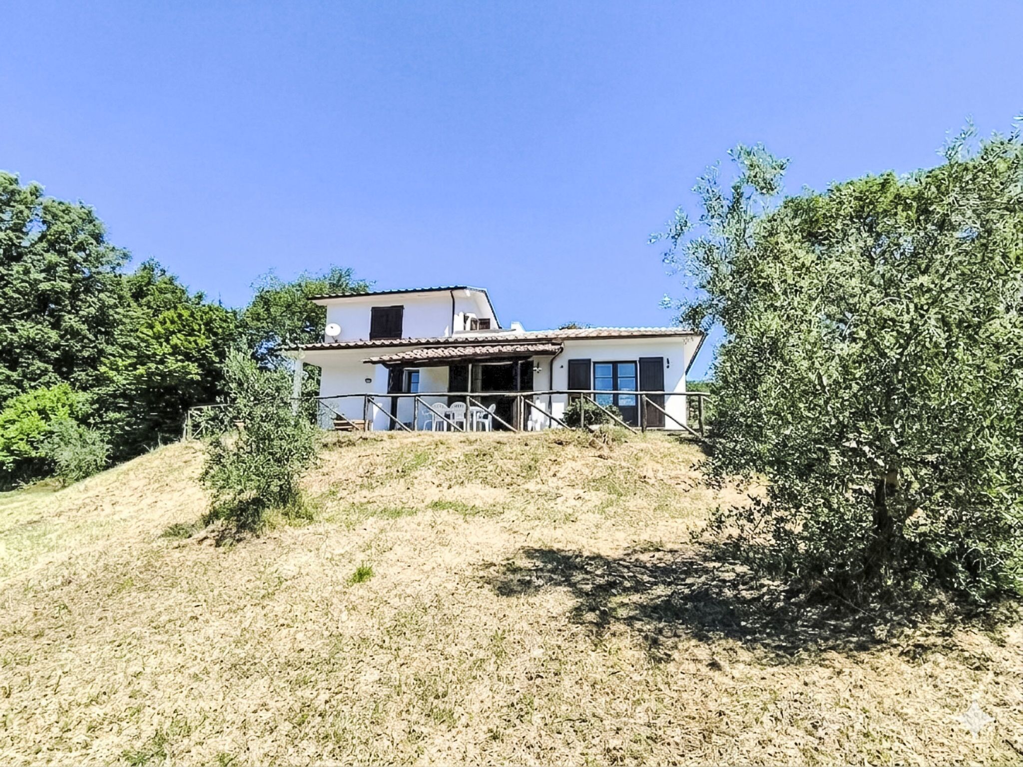 Ein zweistöckiges Haus mit Terrasse und Sitzgelegenheit.