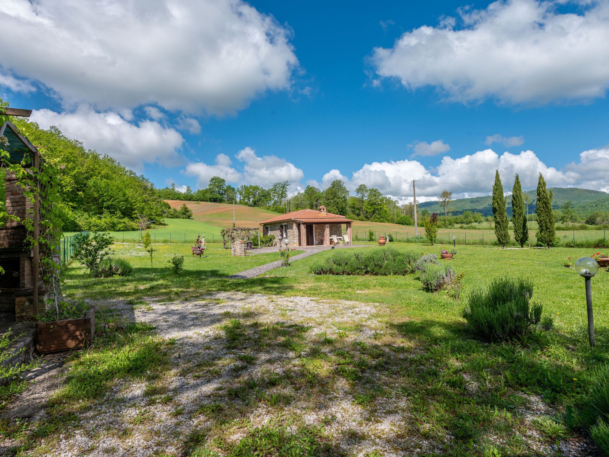 A rustic stone house with a tiled roof, surrounded by a lush green landscape and rolling hills.
