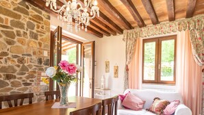 A rustic room with a stone wall, wooden dining table, and a white sofa with pink cushions. - Vacation home Dilia by Interhome (Boccheggiano)
