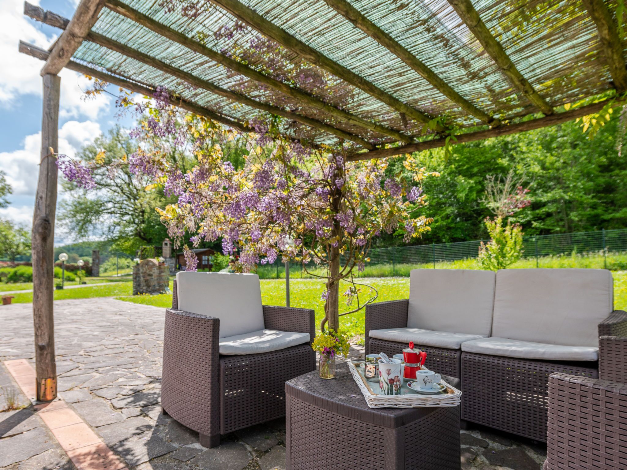 Un área de estar al aire libre techada con muebles de mimbre y una mesa dispuesta con una bandeja de objetos.