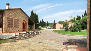 A stone building with a red door, a paved courtyard, and a car parked in the distance. - Le Palaie - 'Oliveto' by Interhome (Peccioli)