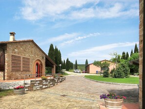 Stroll through the serene courtyard, surrounded by lush greenery and vibrant flowers, to the traditional building with a charming entrance.