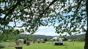 Uma área ao ar livre com gramado, uma única cadeira de descanso, vários guarda-sóis e um gazebo.