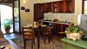 Uma cozinha acolhedora com armários de madeira, uma mesa de jantar com cadeiras e uma televisão sobre um suporte verde.