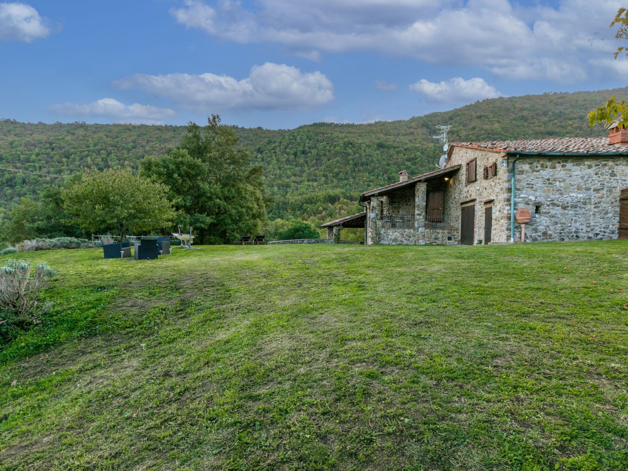Un edificio de piedra con techo inclinado, rodeado de un campo cubierto de hierba y árboles.