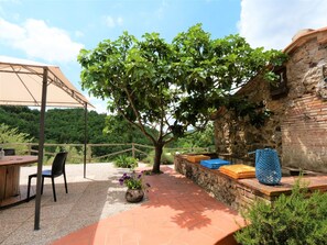 Un patio exterior con mesa y sillas, una pérgola, un árbol y una pared de piedra.