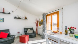 Uma sala de estar moderna com um sofá, um banquinho vermelho, uma mesa de jantar com cadeiras e uma janela com cortinas.