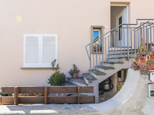 A residential building with a wooden bench, potted plants, and a staircase leading to an upper level.