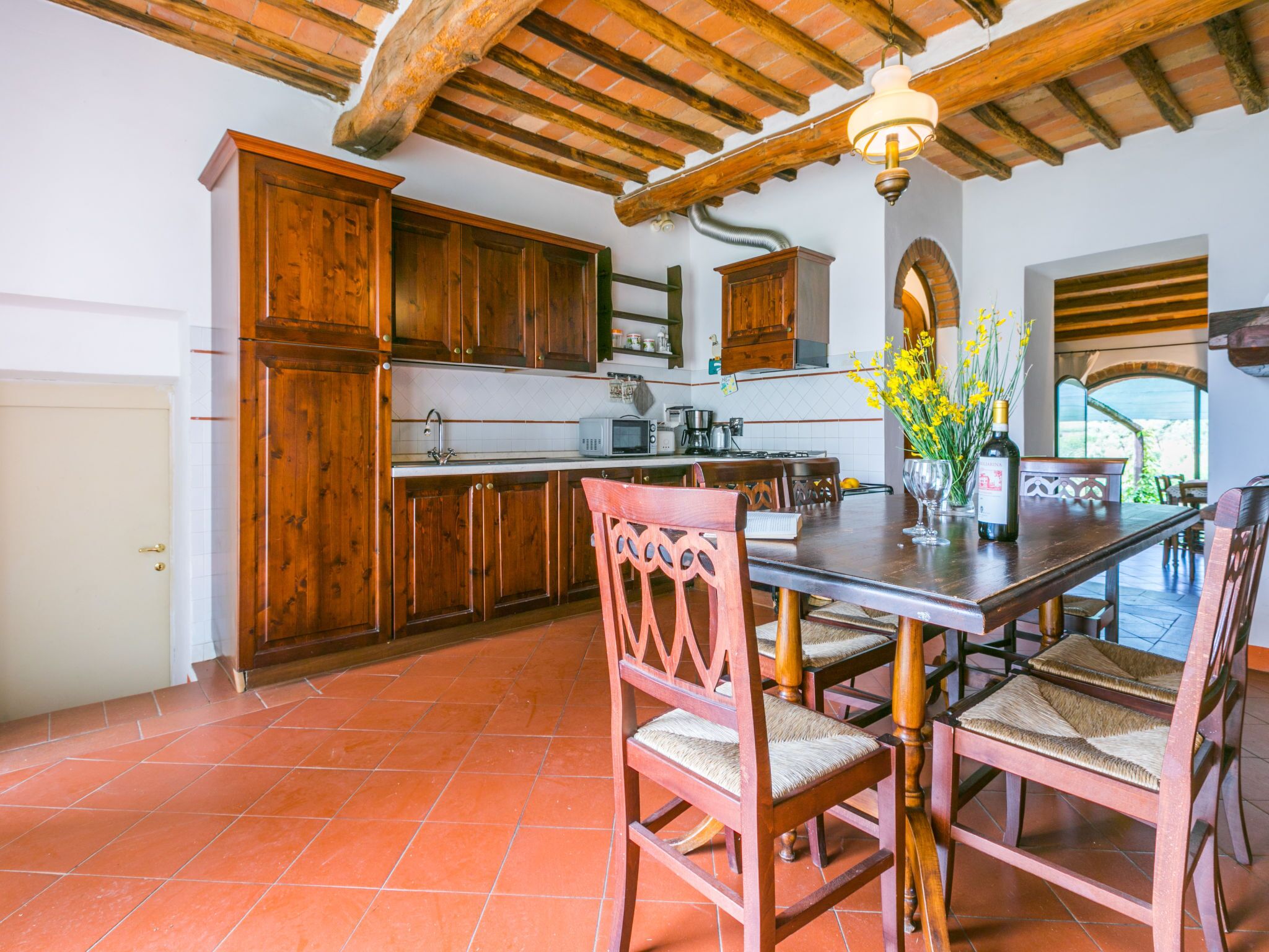 A rustic kitchen with wooden cabinets, a tiled floor, and a dining area with wooden chairs and a table.