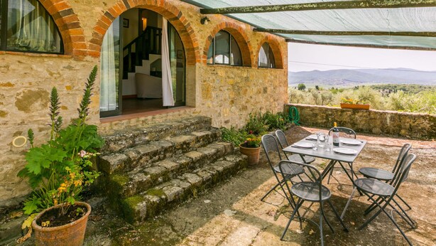 A rustic stone building with a covered patio, outdoor seating, and a view of the countryside.