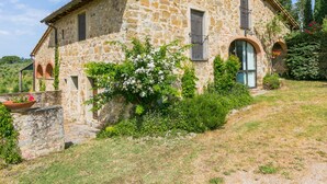 A stone house with a sloped roof, a small porch, and a garden with flowering plants.