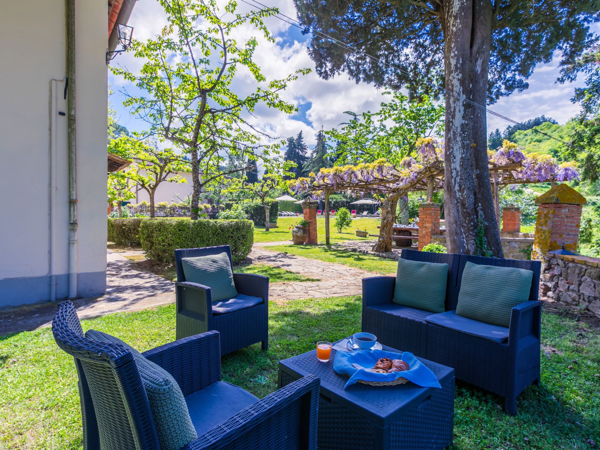 Un espacio al aire libre con mobiliario de mimbre y una mesa dispuesta con una bebida y pasteles.