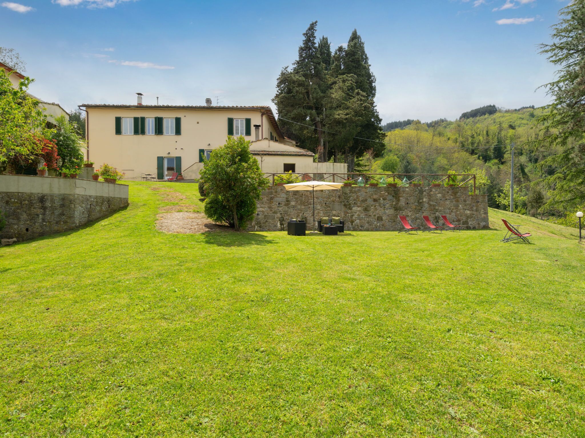 A house with a stone wall, a lawn, and a view of the surrounding hills.