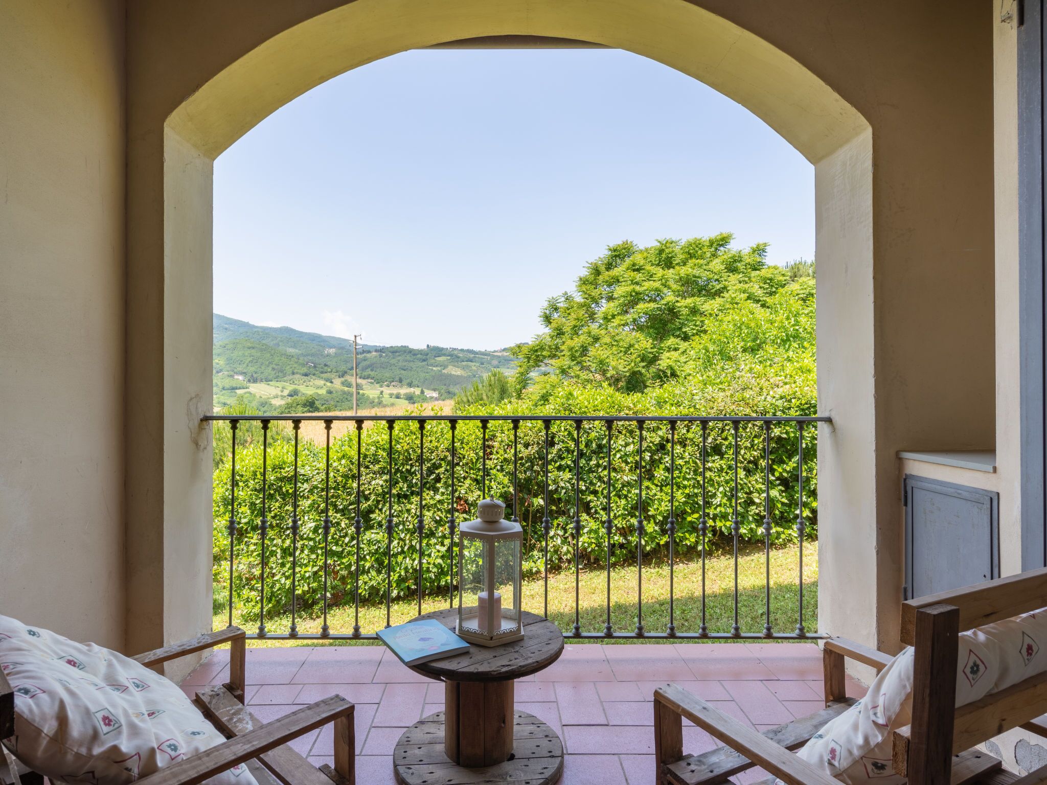 A balcony with a view of a green landscape, a table with a candle, and two chairs.