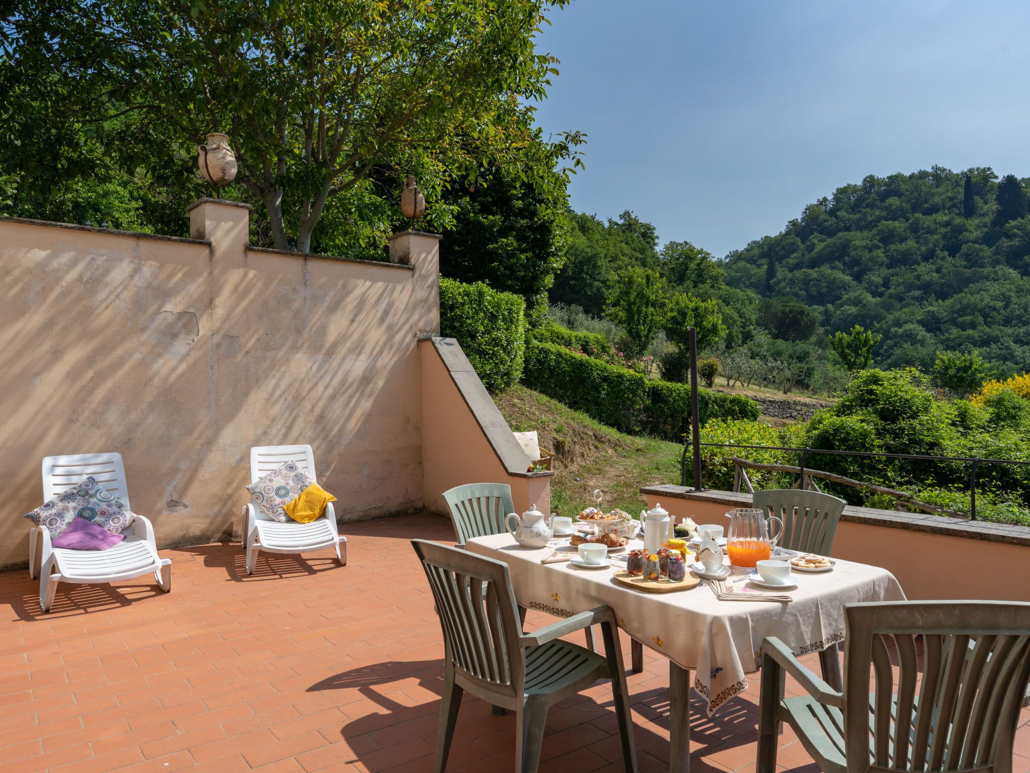 Un área de comedor al aire libre con una mesa dispuesta para el desayuno, rodeada de sillas y con vistas a un paisaje montañoso y exuberante.