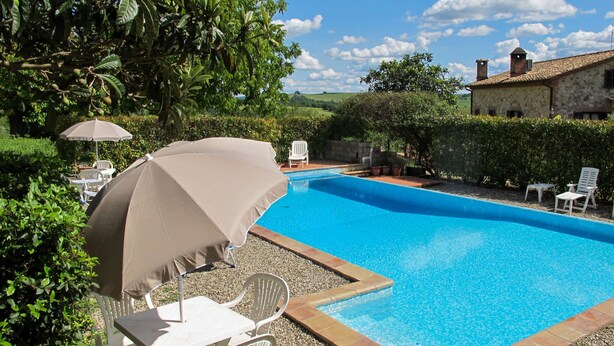 A swimming pool with a clear blue water, surrounded by a stone wall, and a white chair and umbrella.