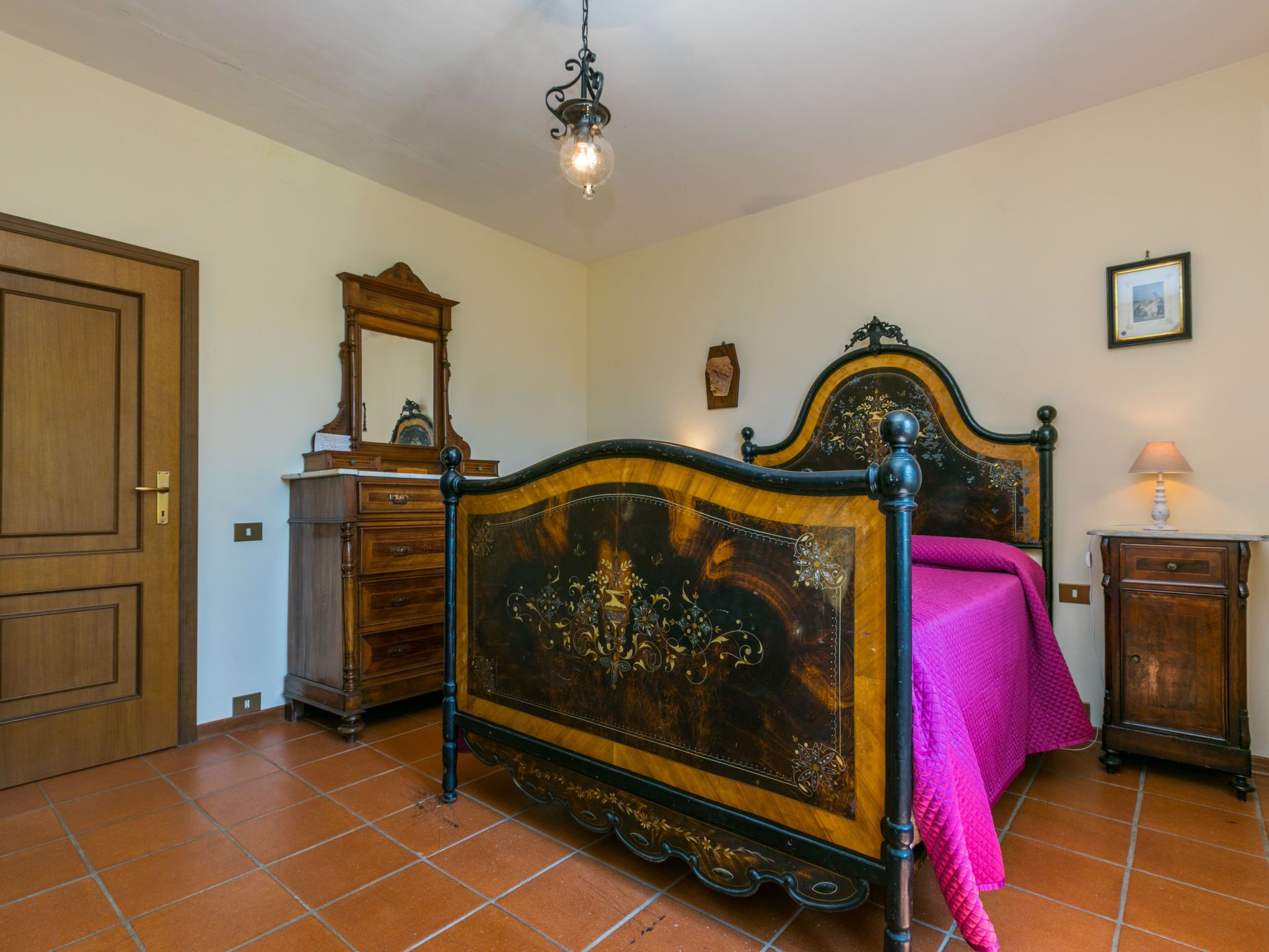 Una camera da letto con un letto di legno, una cassettiera, uno specchio, una lampada e una porta.