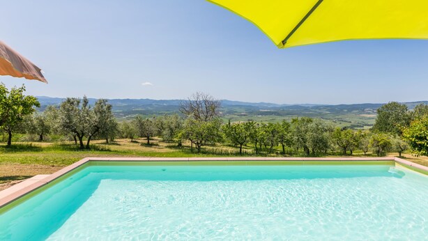 Une piscine d’un bleu éclatant, surmontée d’un parasol jaune, entourée d’un paysage luxuriant et bordée de collines lointaines.