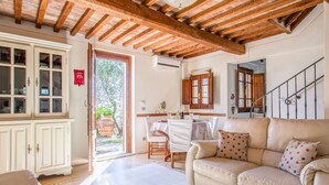 A cozy living room with a wooden ceiling, a beige sofa, a dining table with chairs, and a kitchen area with wooden cabinets and a window. - Vacation home Iacopo by Interhome (Montecatini Terme)