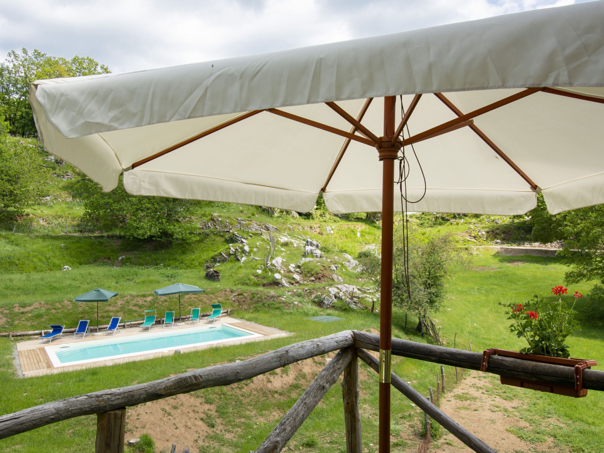 A pool area with a wooden deck, a white umbrella, and green lounge chairs.