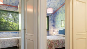 Ein Schlafzimmer mit zwei Betten, einem Fenster mit Blick auf Grünflächen und einer Decke, die mit einem blauen abstrakten Muster bemalt ist.