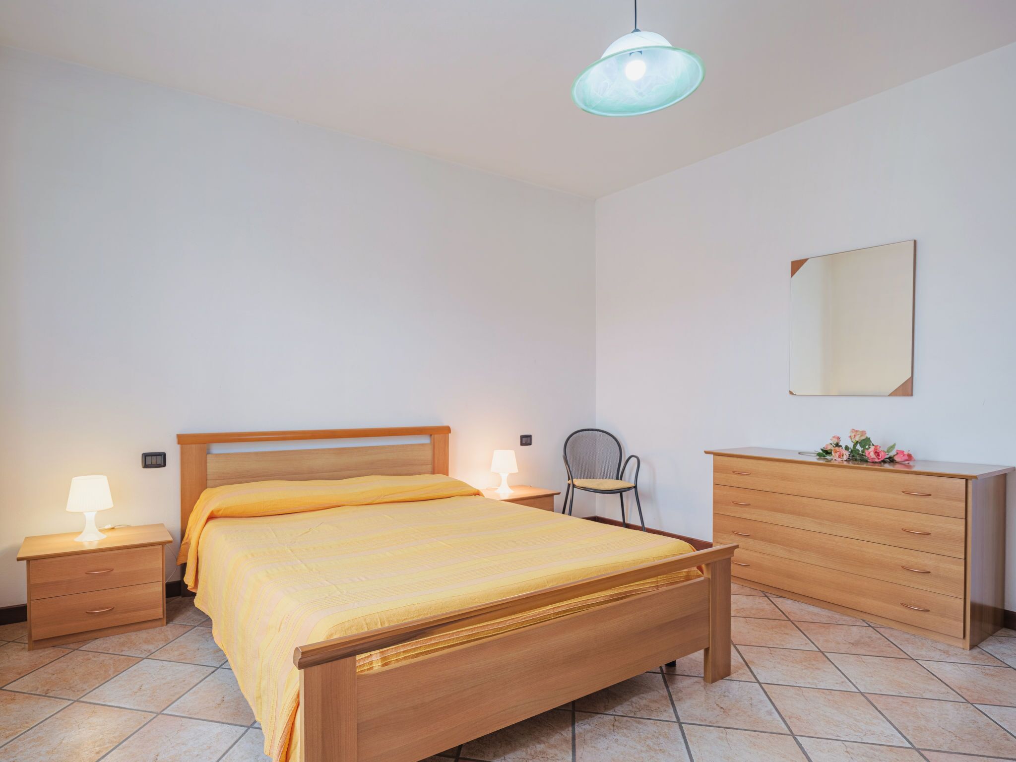 A bedroom with a wooden bed, nightstands, a chair, a dresser, and a hanging light fixture.