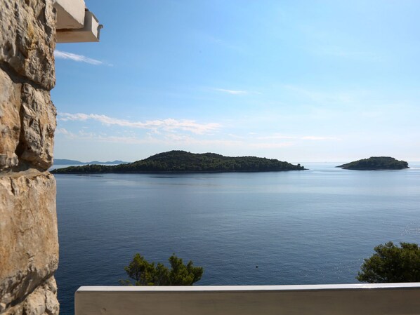 A view of a calm sea with two small islands, a stone building on the left, and a clear sky.