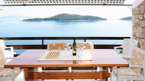 A wooden table set with wine glasses and a bottle, overlooking a calm sea and a green island.