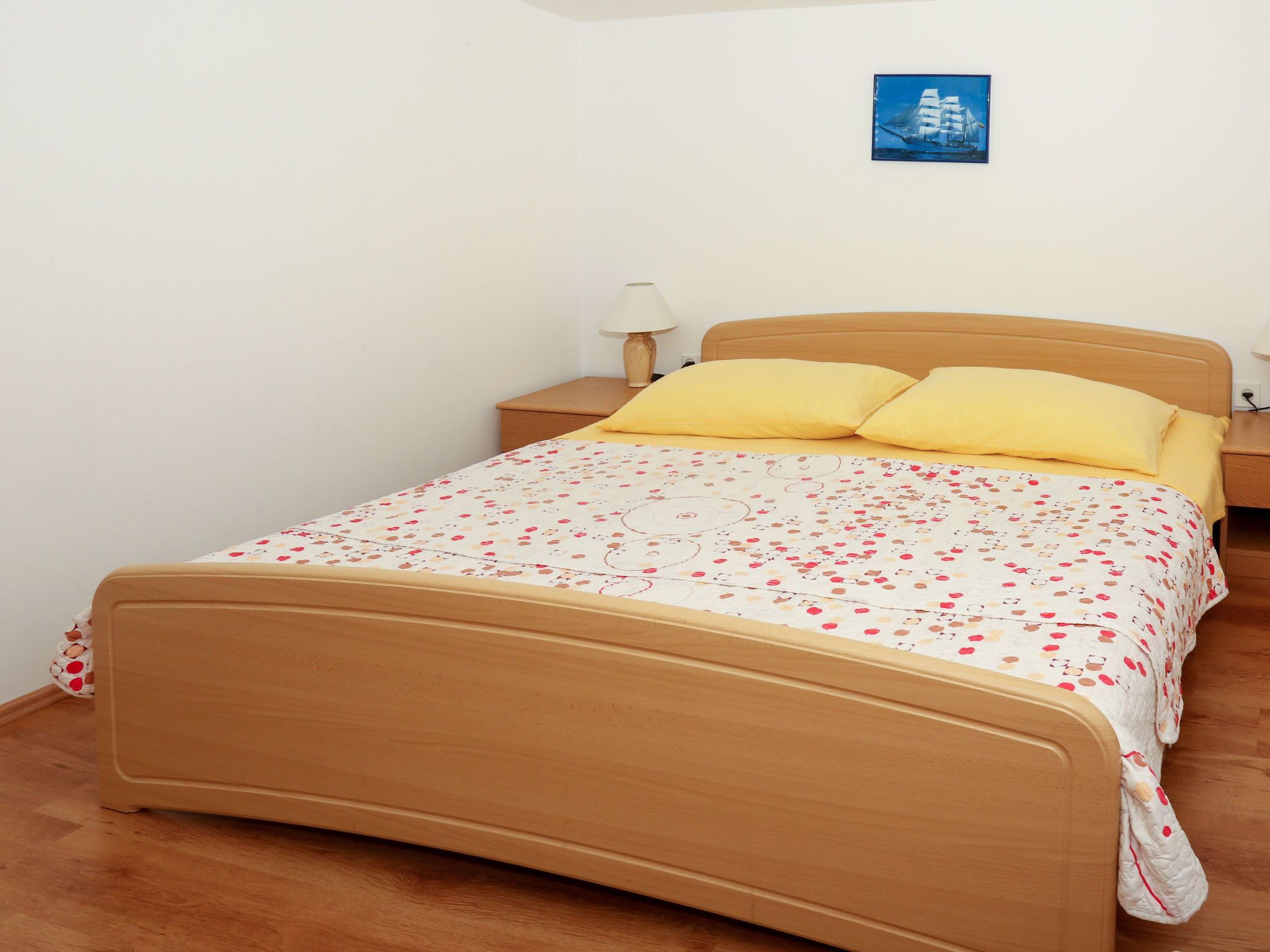 A bedroom with a wooden bed, a nightstand, a lamp, and a framed picture on the wall.