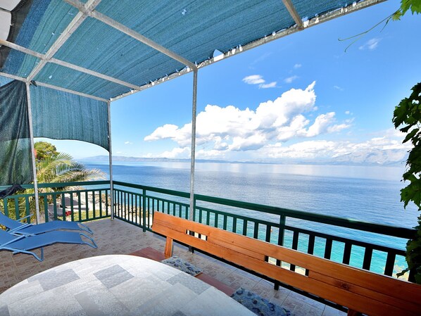 A balcony with a view of the sea, a wooden bench, and a table with a patterned tablecloth.