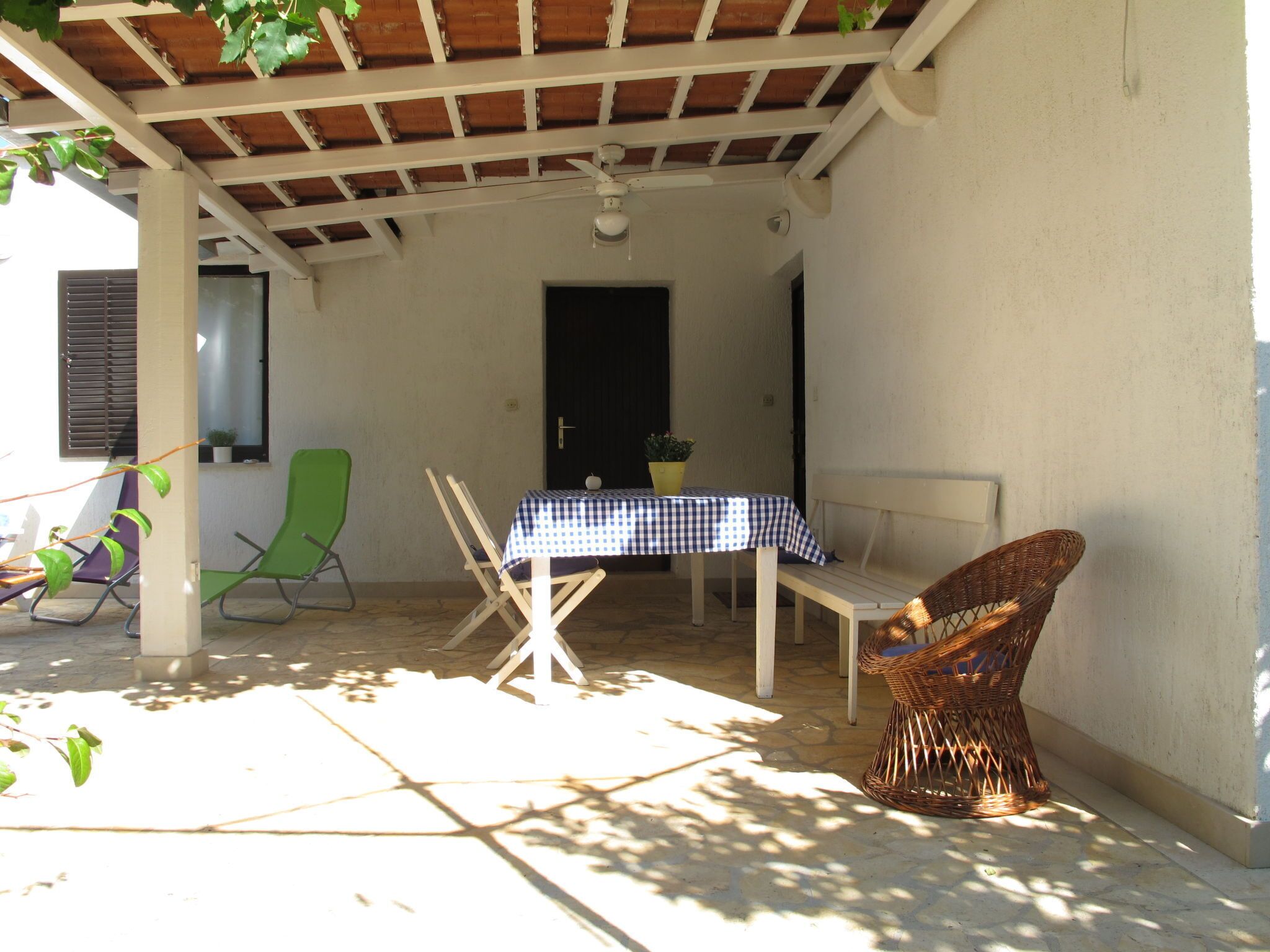 An outdoor patio with a table covered by a checkered tablecloth, a wicker chair, and a green lounge chair.