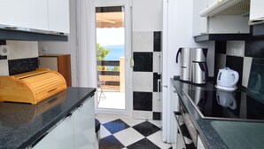 A compact kitchen with a checkered floor, a wooden cutting board, a coffee maker, and a view of the sea through a door. - Apartment Nina by Interhome (Omiš)
