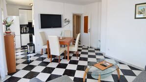 A modern living room with a checkered floor, a dining area with a wooden table and chairs, a flat-screen TV mounted on the wall, and a small glass table with a remote control. - Apartment Nina by Interhome (Omiš)