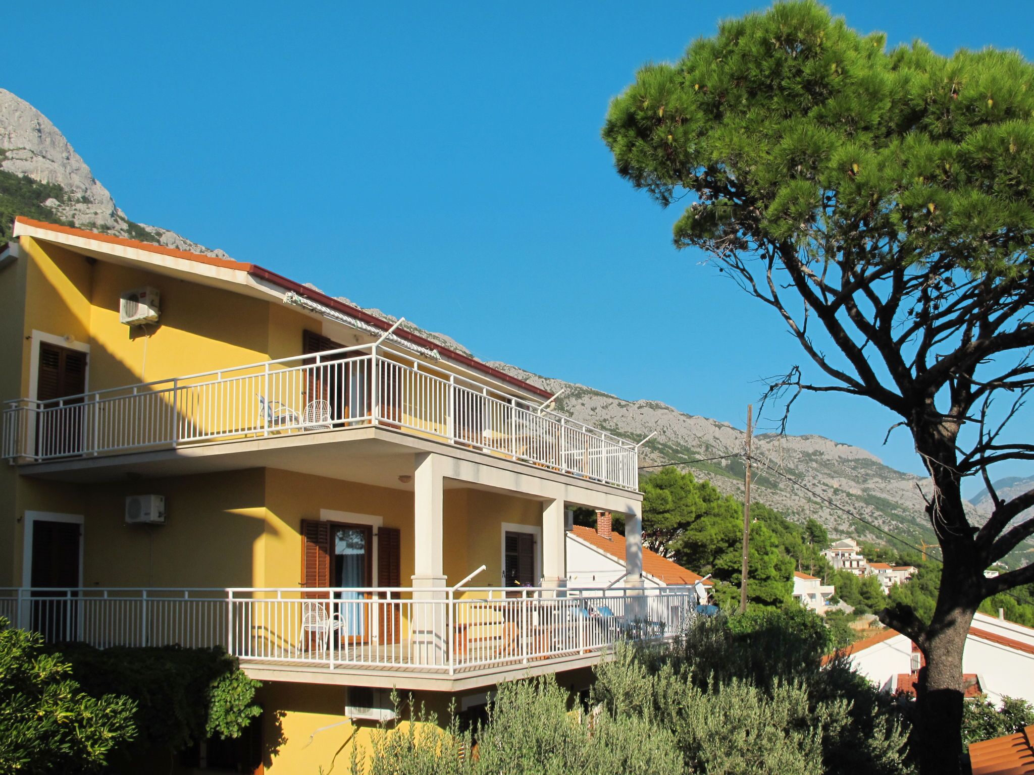 A two-story building with balconies, surrounded by greenery and mountains.