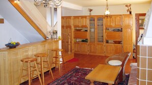 A spacious kitchen with wooden cabinets, a bar area with stools, a patterned rug, and a dining area with a table and chairs.