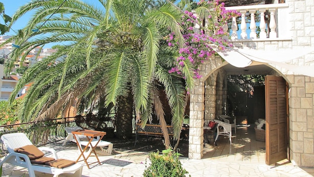 A patio area with lounge chairs and a table, surrounded by palm trees and a stone wall.