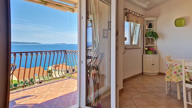 Een balkon met uitzicht op zee, een schuifdeur, een stoel, een klein tafeltje en een kast.
