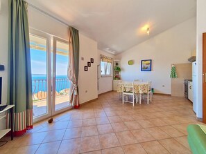 Een kamer met balkon, eettafel, keukenhoek en uitzicht op zee.